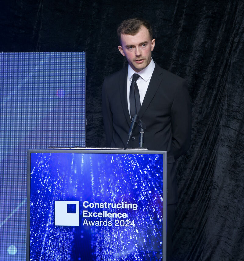Man in a dark suit and tie speaks at a podium on stage during the Constructing Excellence Awards 2024.